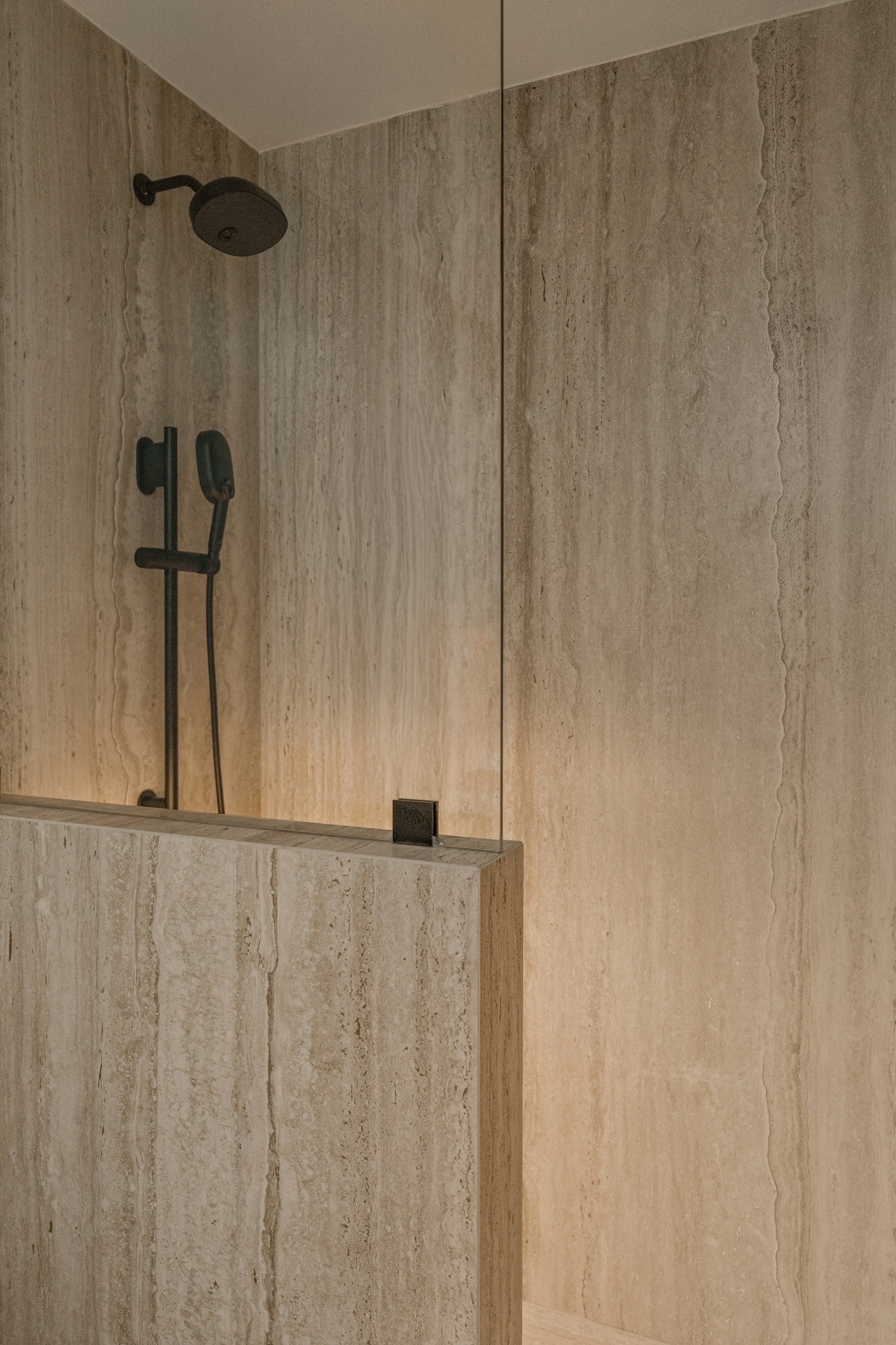 The bathroom: travertine cladding in broad horizontal bands, lit along the slab by a concealed warm strip.