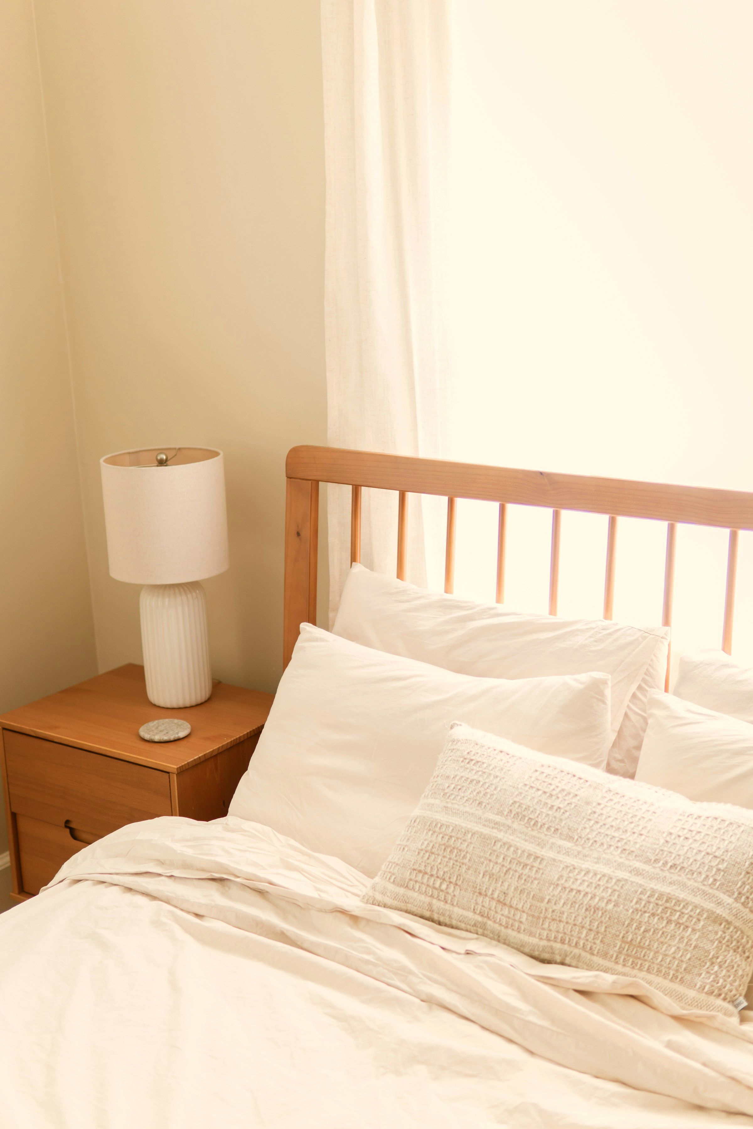 The bedroom: white linen bedding against an oak spindle headboard, beside a sheer linen curtain full of daylight.