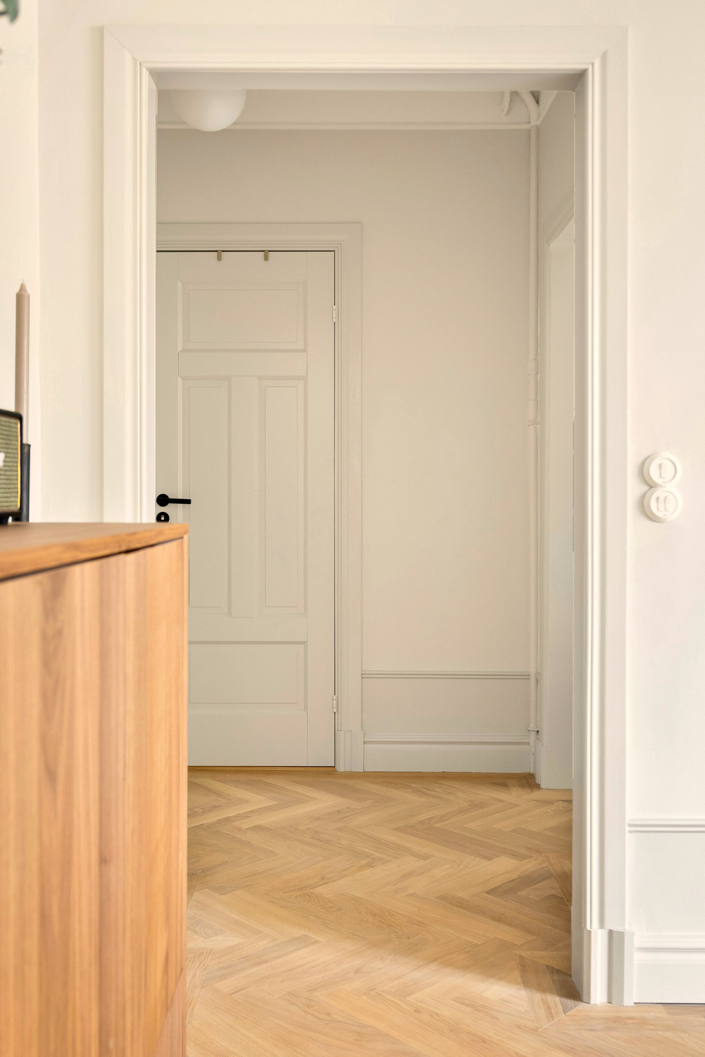 The entry hall: pale oak herringbone running through a wide cased opening, moulded architraves and dado, a curved oak cabinet and an opal globe pendant.