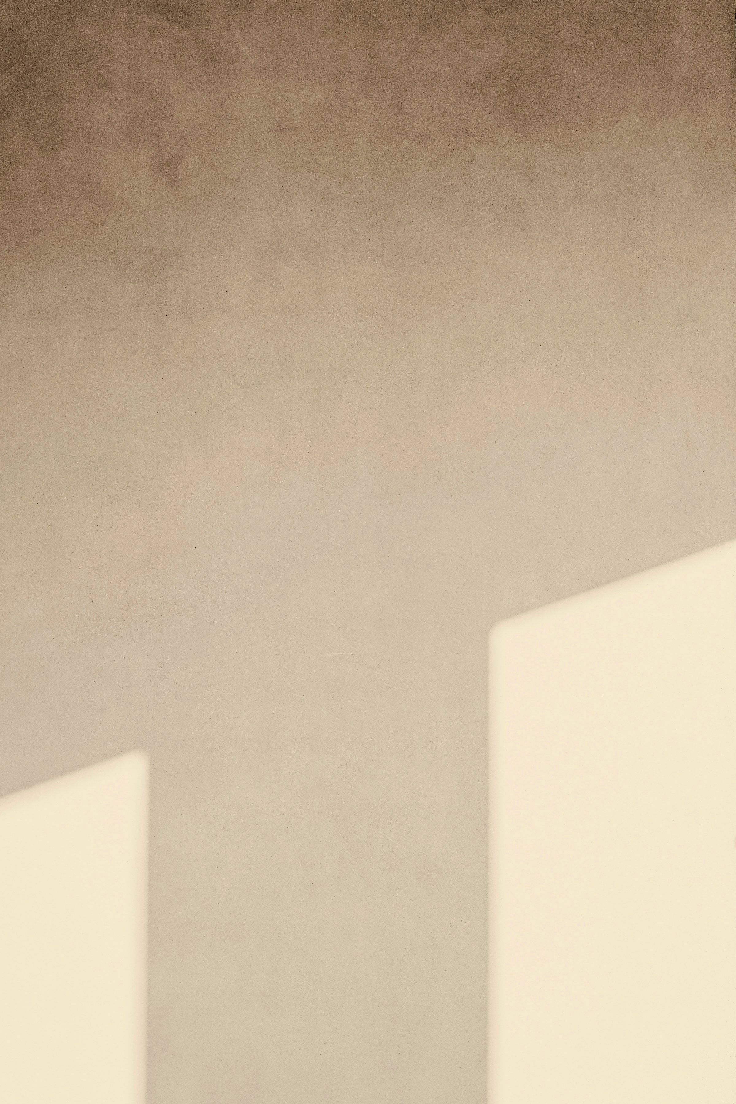 A bare warm plaster wall in the studio with two soft patches of afternoon daylight lying across it.