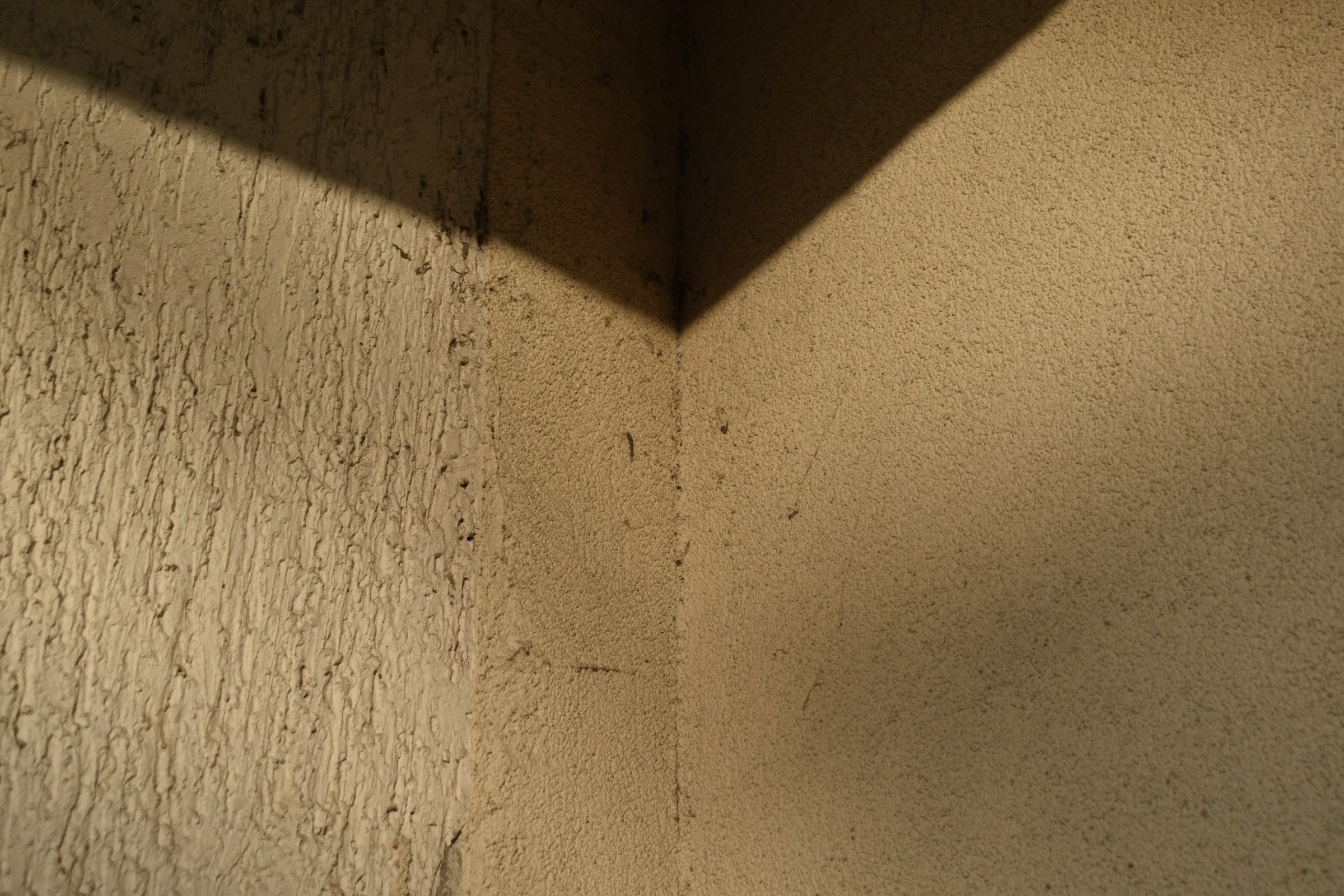 Two trowelled lime-plaster walls meeting at an internal corner under sharp raking sunlight.