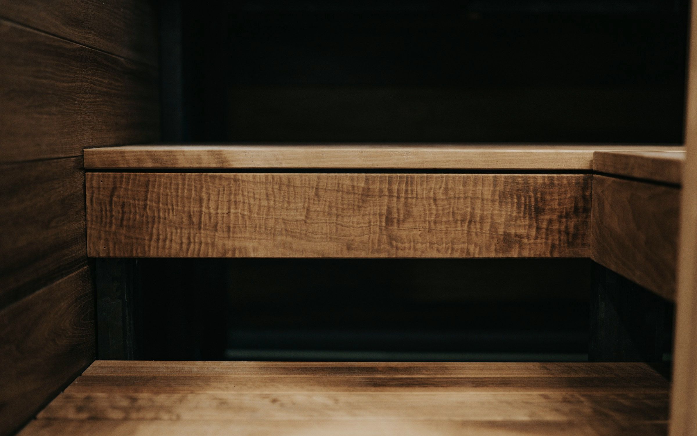 Close-up of an oiled smoked-oak joinery corner, the figured grain raking away into shadow.