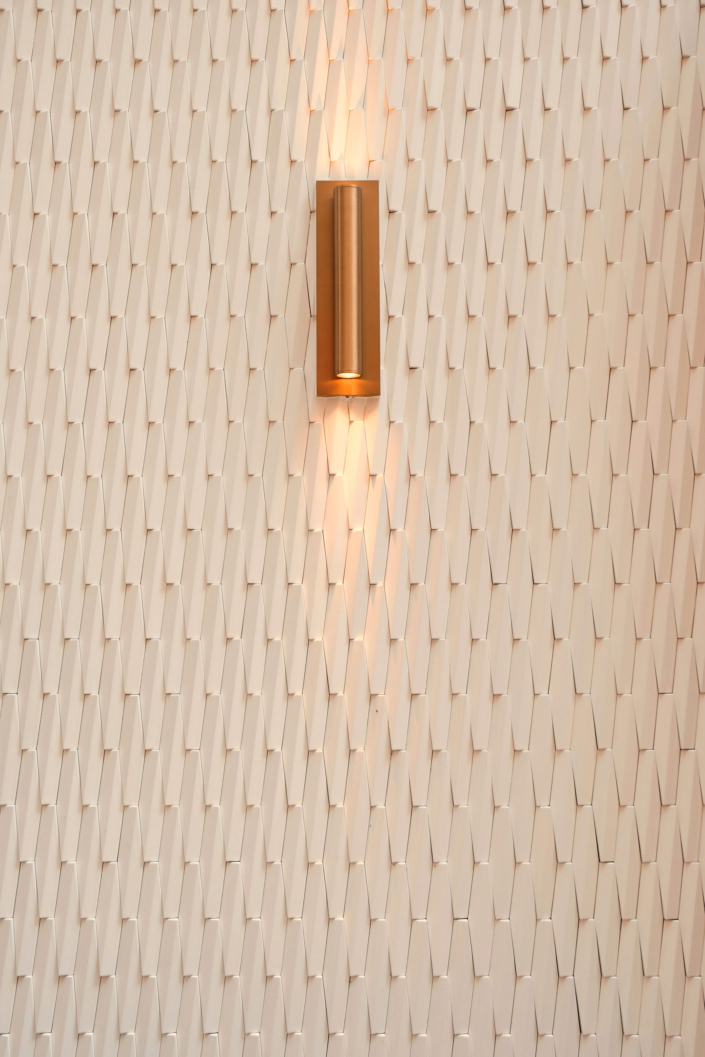 Brass fixture close-up: a wall light glowing against a textured white plaster relief.