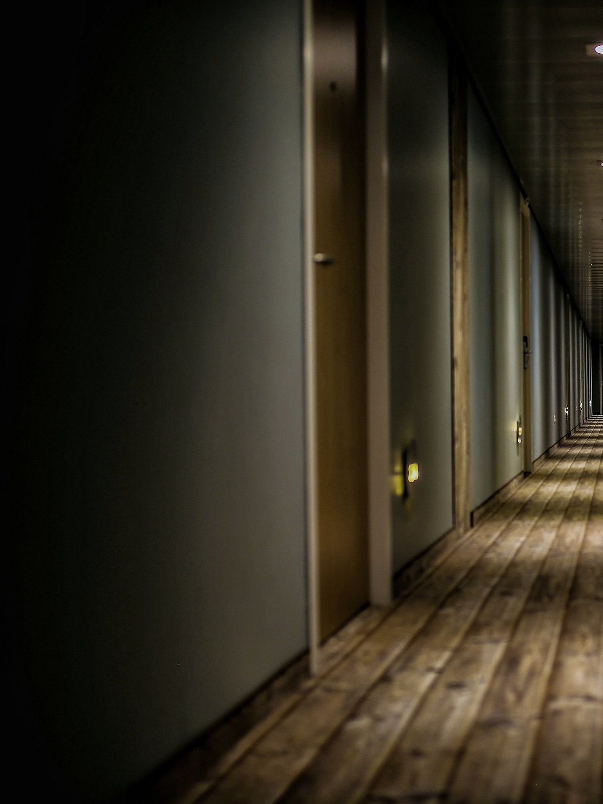 A guest corridor at night: low wall washers throwing light down a reclaimed plank floor between oak doors.