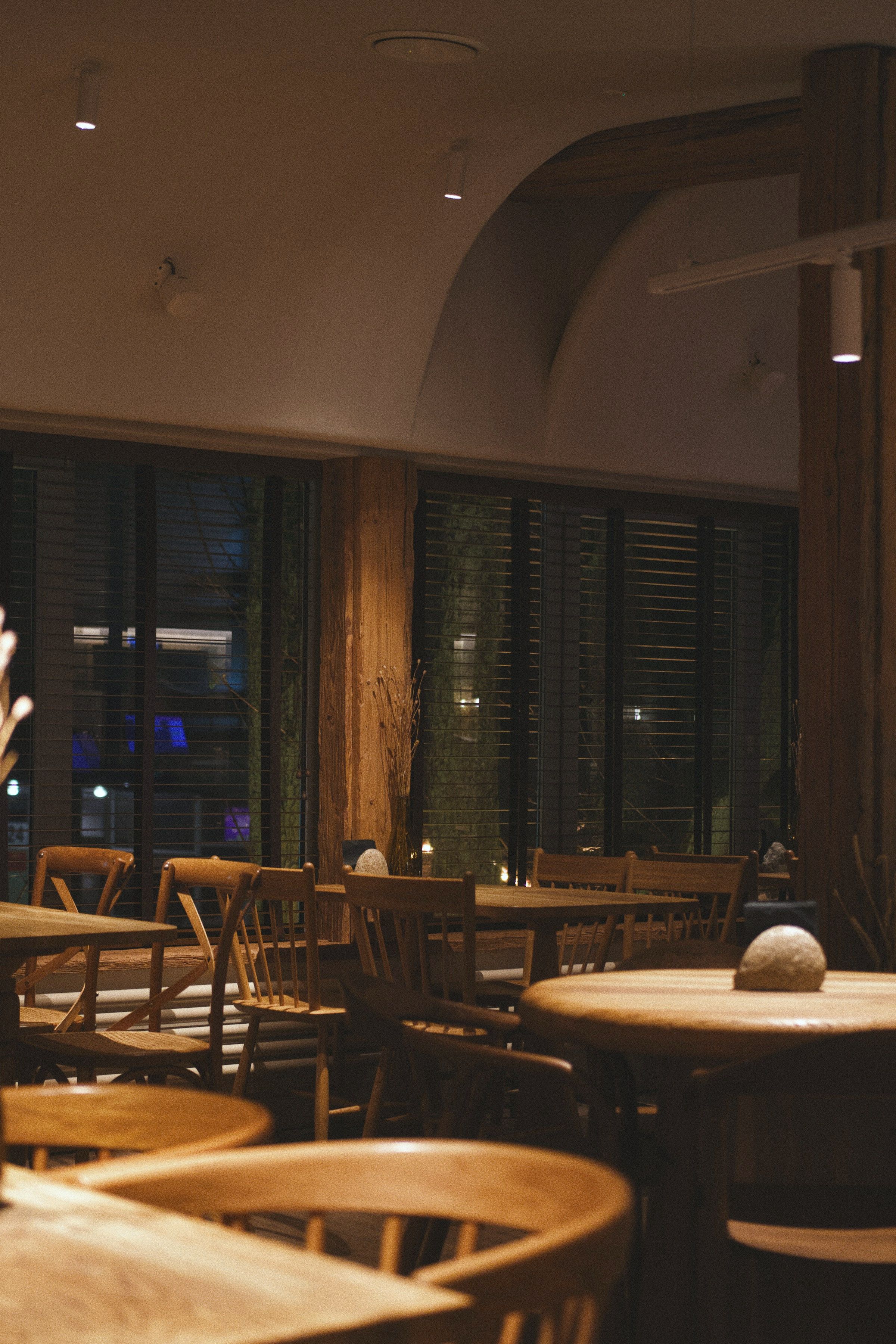 The restaurant in evening light: oak tables laid and waiting, plaster walls, dark windows and warm lamps.
