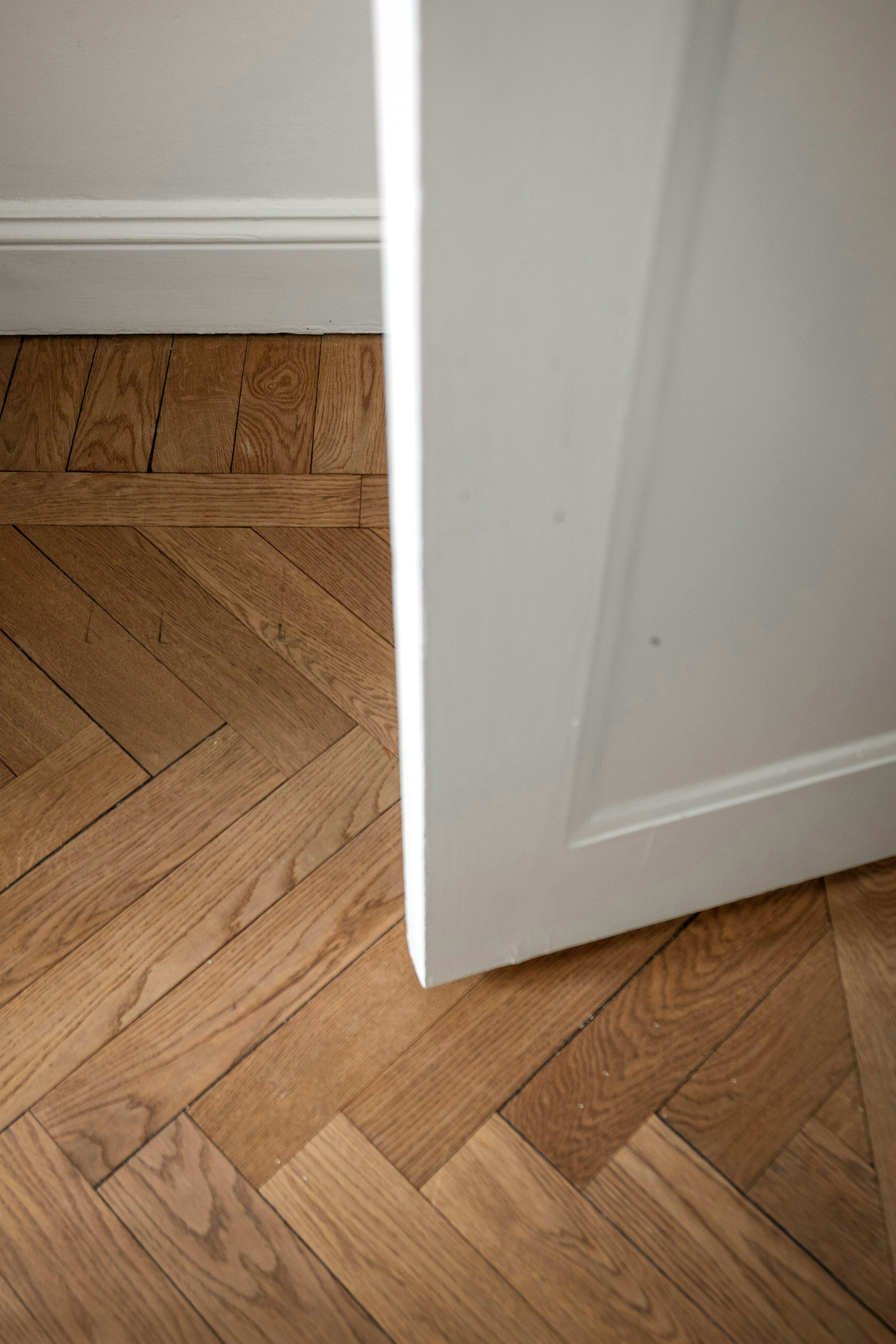 Oak herringbone parquet running up to the panelled door and painted skirting of a restored Frederiksstaden apartment, in soft daylight.