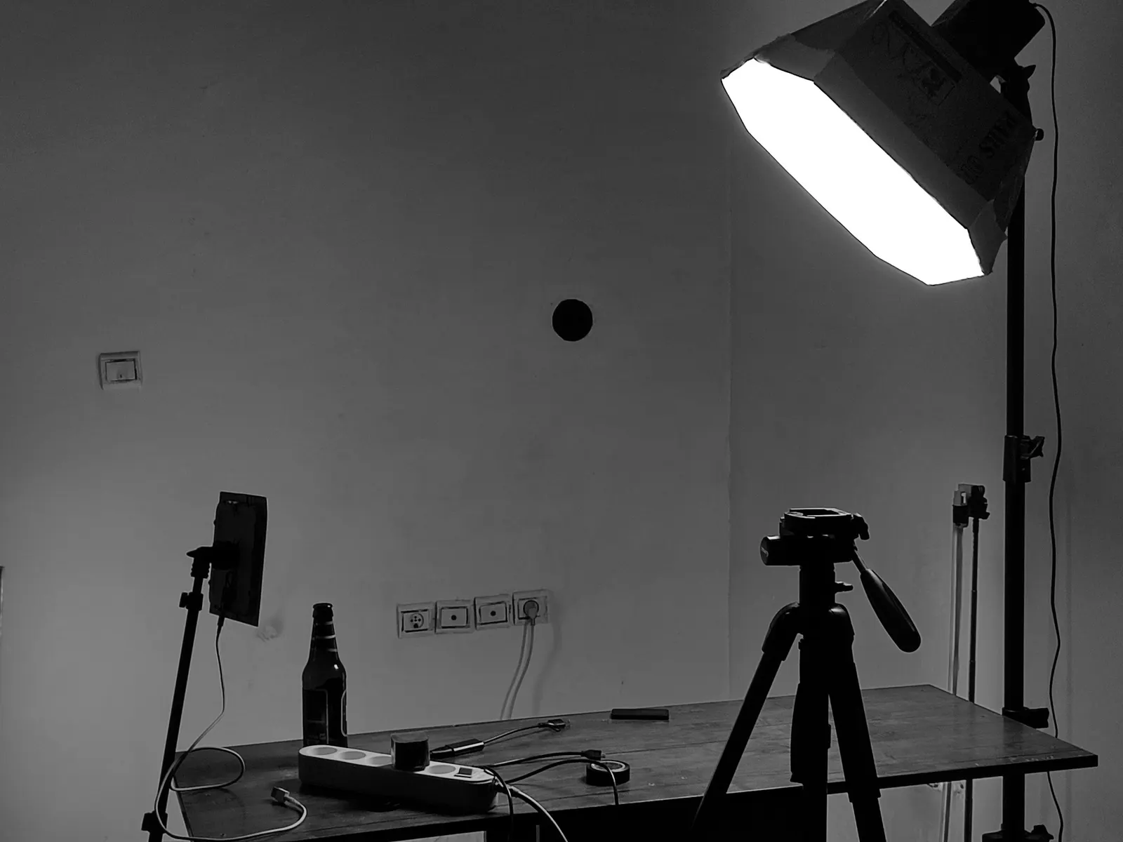A desk, a tripod and a softbox in a plain room