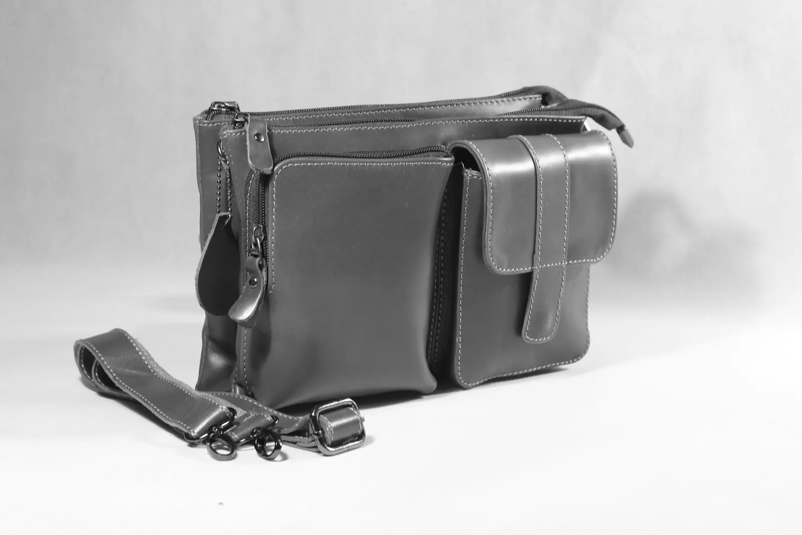 A leather camera bag with its strap on a pale background