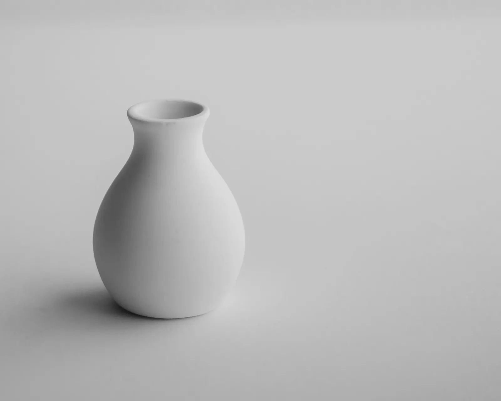 A single matte white porcelain bud vase on white