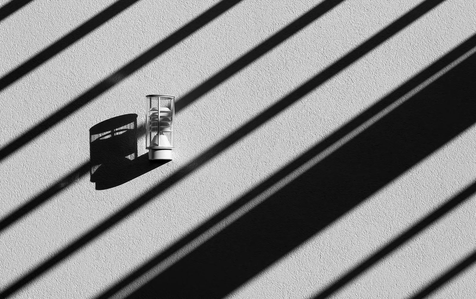 A small glass on a table striped with hard shadows from a blind