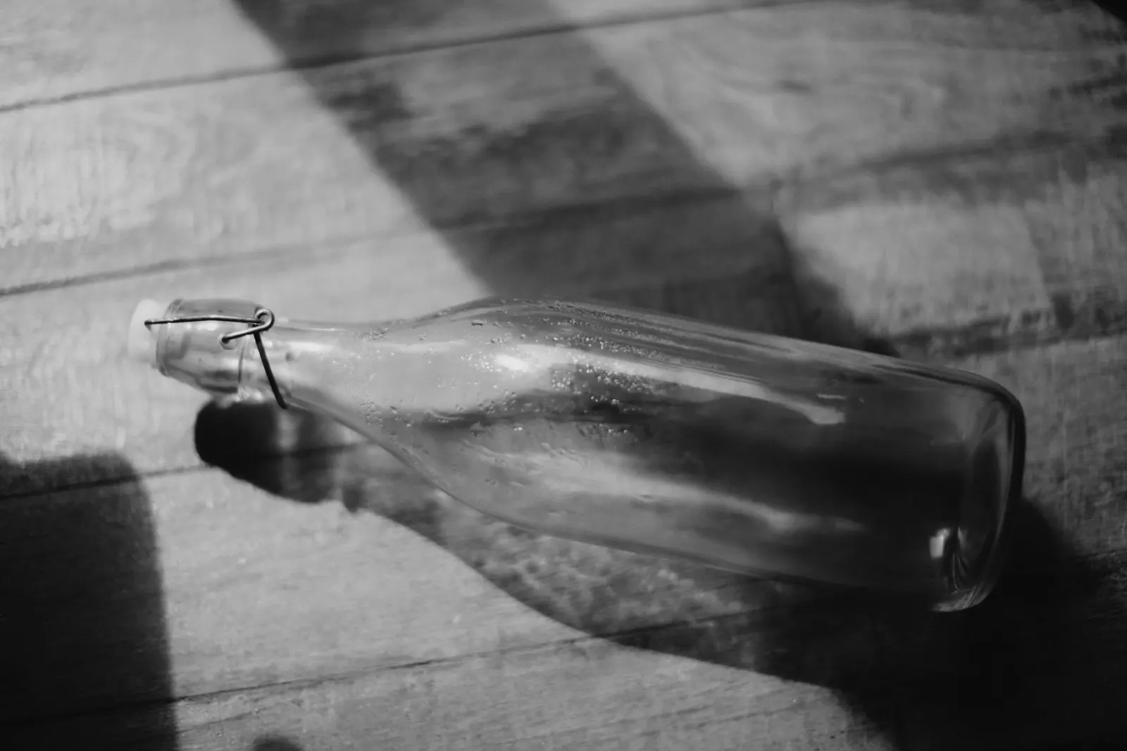 A swing-top glass bottle lying on a wooden floor in sunlight