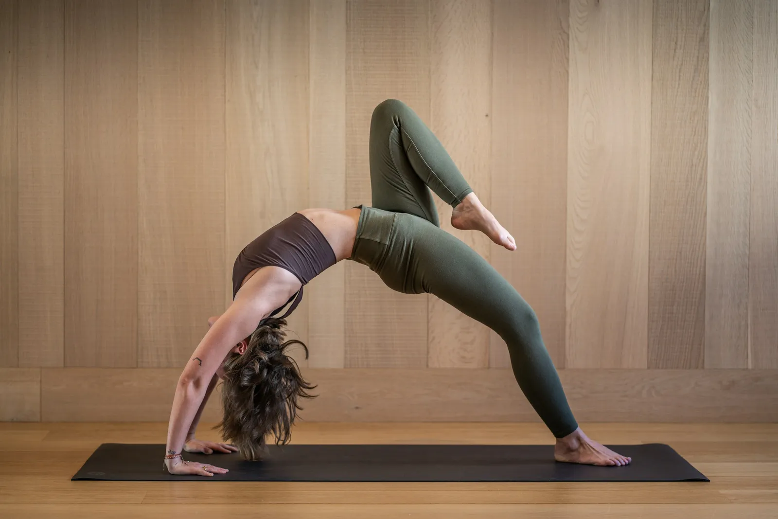 A woman holding a yoga backbend on a mat in a warm wooden studio