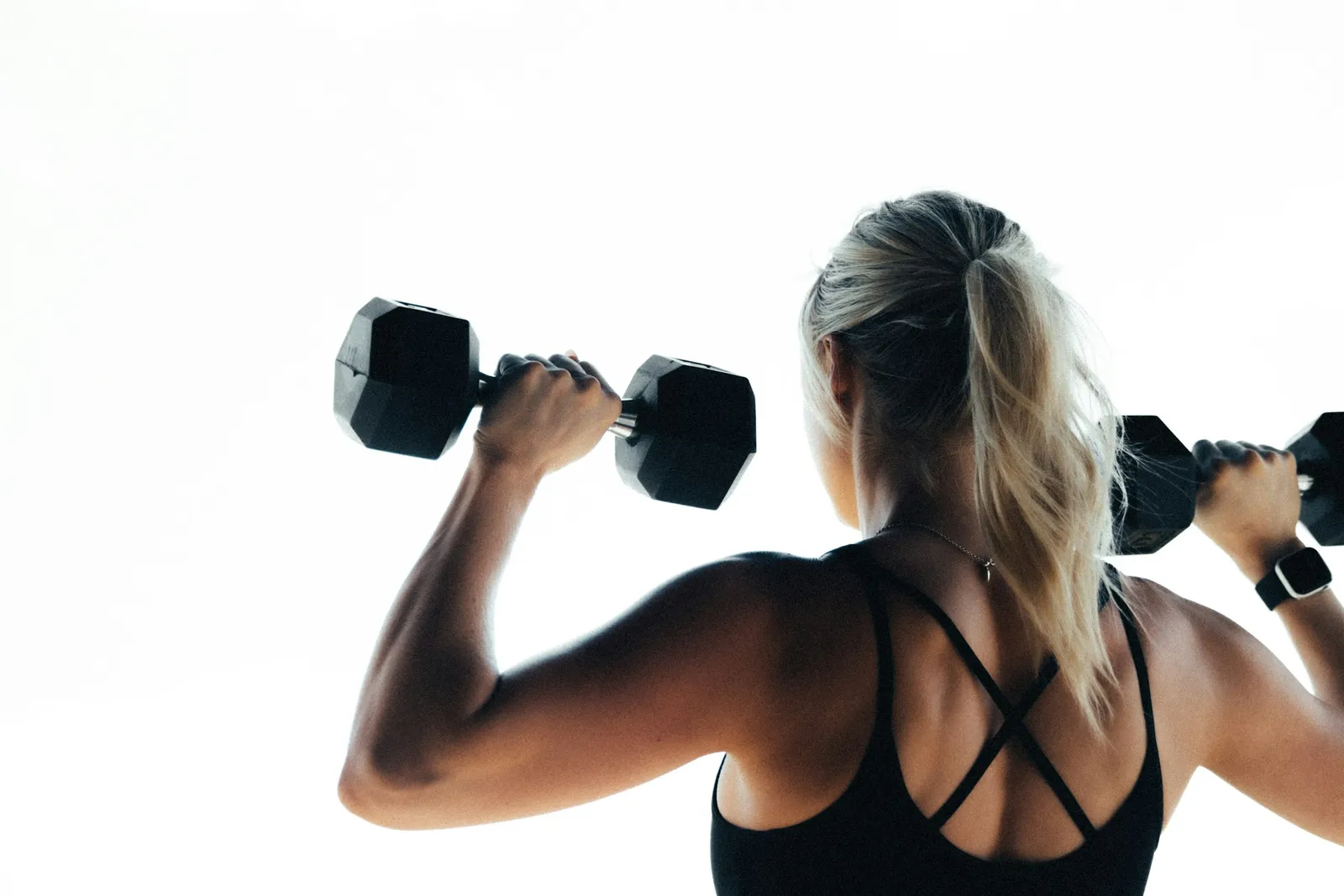 A woman pressing two dumbbells overhead